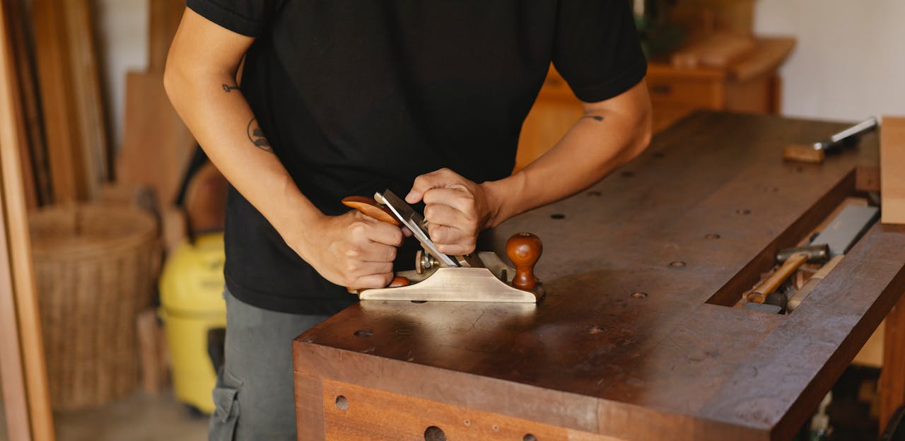 Woodworker focuses on smoothing wood with a planer in a cozy workshop setting.